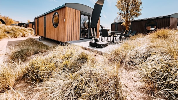A modern building with a wooden exterior, a circular window, and a dining area with outdoor seating. - Holiday Home 'Kaperfahrt' with Private Terrace, Wi-Fi and Air Conditioning (Großenbrode)