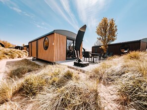 A modern building with a wooden exterior, a circular window, and a dining area with outdoor seating. - Holiday Home 'Kaperfahrt' with Private Terrace, Wi-Fi and Air Conditioning (Großenbrode)
