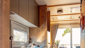 A compact kitchen with wooden cabinetry, a built-in microwave, and a dining area with a table and chairs. - Holiday Home 'Kaperfahrt' with Private Terrace, Wi-Fi and Air Conditioning (Großenbrode)