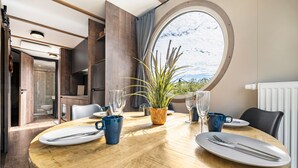 A round dining table with plates, cutlery, and blue mugs, surrounded by chairs, with a large window and a plant in the center. - Holiday Home 'Kaperfahrt' with Private Terrace, Wi-Fi and Air Conditioning (Großenbrode)