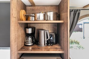 A wooden shelf unit with kitchen appliances including a coffee maker, a kettle, and pots.