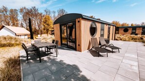 A modern outdoor patio with a wooden structure, a dining table with chairs, and lounge chairs. - Holiday Home 'Kaperfahrt' with Private Terrace, Wi-Fi and Air Conditioning (Großenbrode)