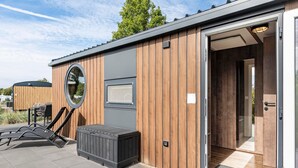 A modern building with a wooden exterior, a large circular window, and a door leading inside. - Holiday Home 'Kaperfahrt' with Private Terrace, Wi-Fi and Air Conditioning (Großenbrode)