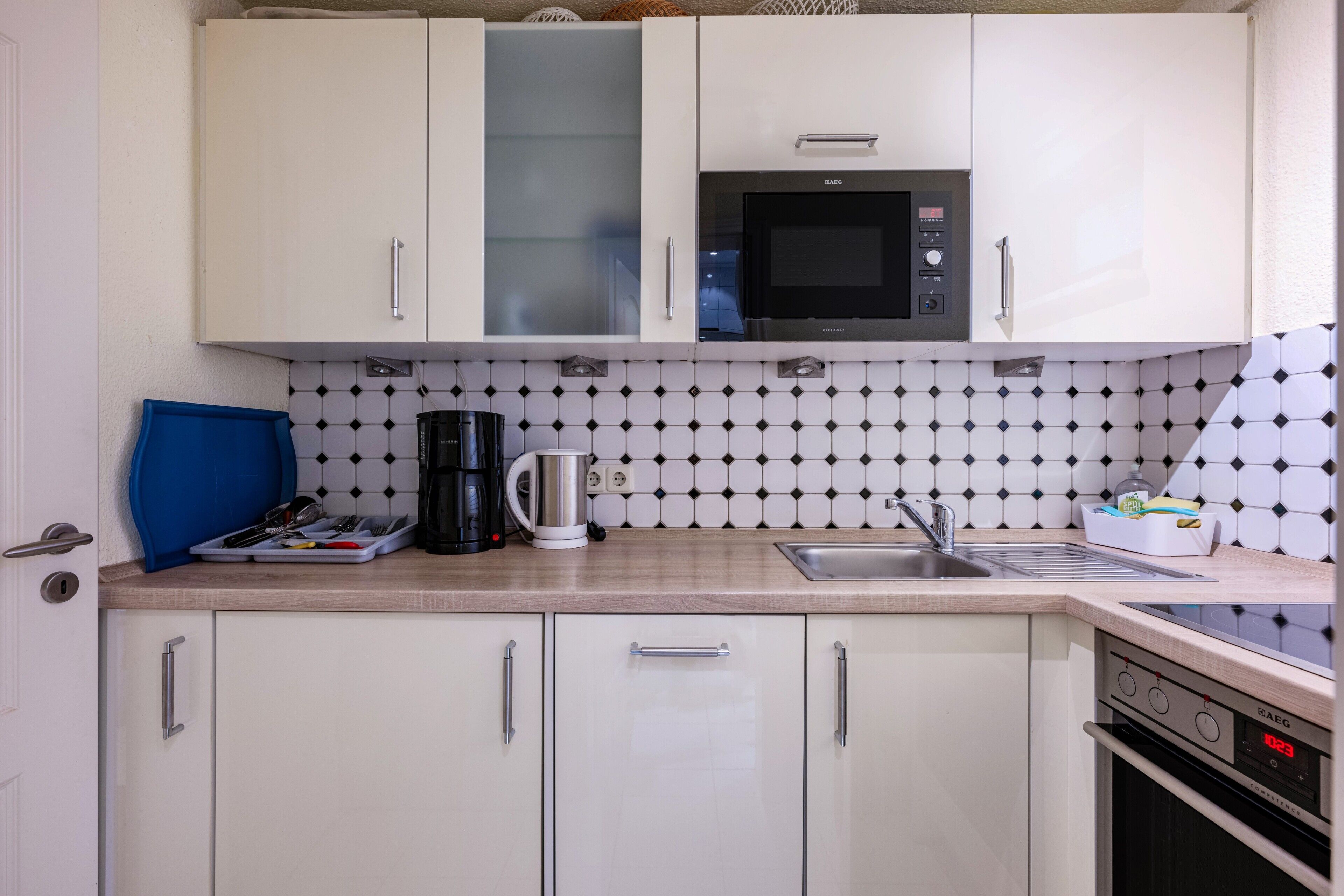 A kitchen with white cabinets, a microwave, a coffee maker, and a sink.