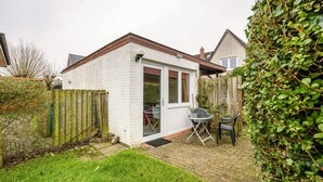 Une petite maison blanche avec une terrasse en briques, une clôture en bois et un jardin.