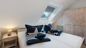 Ein Schlafzimmer mit Dachfenster, einem Bett mit gestreifter Bettwäsche, einem Nachttisch mit Lampe und einem Kleiderschrank.