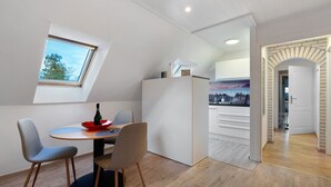 Ein modernes Zimmer mit Esstisch, Stühlen, einem kleinen Fenster und einer Tür zu einem weiteren Bereich.