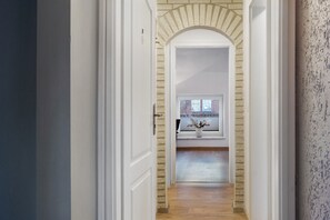 Een gang met een bakstenen boog die leidt naar een kamer met een raam en een vaas op de vensterbank.