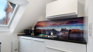 Eine moderne Küche mit Sonnenuntergangsmalerei im Küstenstil, weißen Schränken und einem Fenster mit Blick auf eine Ziegelwand.