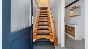 Eine moderne Treppe mit Holzdielen und schwarzen Teppichläufern, die zu einer Zwischenebene mit einer weißen Konsole und einem Spiegel darüber führt.
