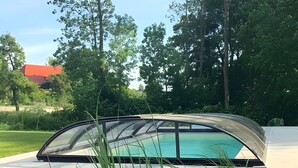 Un área de piscina moderna al aire libre con cerramiento de vidrio, rodeada por un jardín ajardinado con plantas verdes y acolchado.