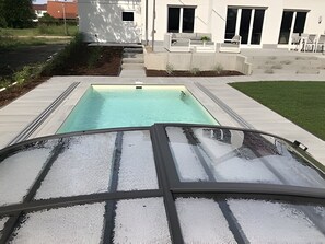 A swimming pool with a glass enclosure, a concrete deck, and a building with large windows in the background. - Villa 'Strandvilla Leni' with Private Pool, Terrace, and Wi-Fi (Kalkhorst)