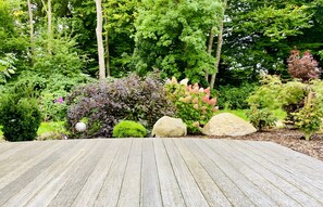 A wooden deck with a garden featuring various shrubs and trees. - Villa 'Strandvilla Leni' with Private Pool, Terrace, and Wi-Fi (Kalkhorst)