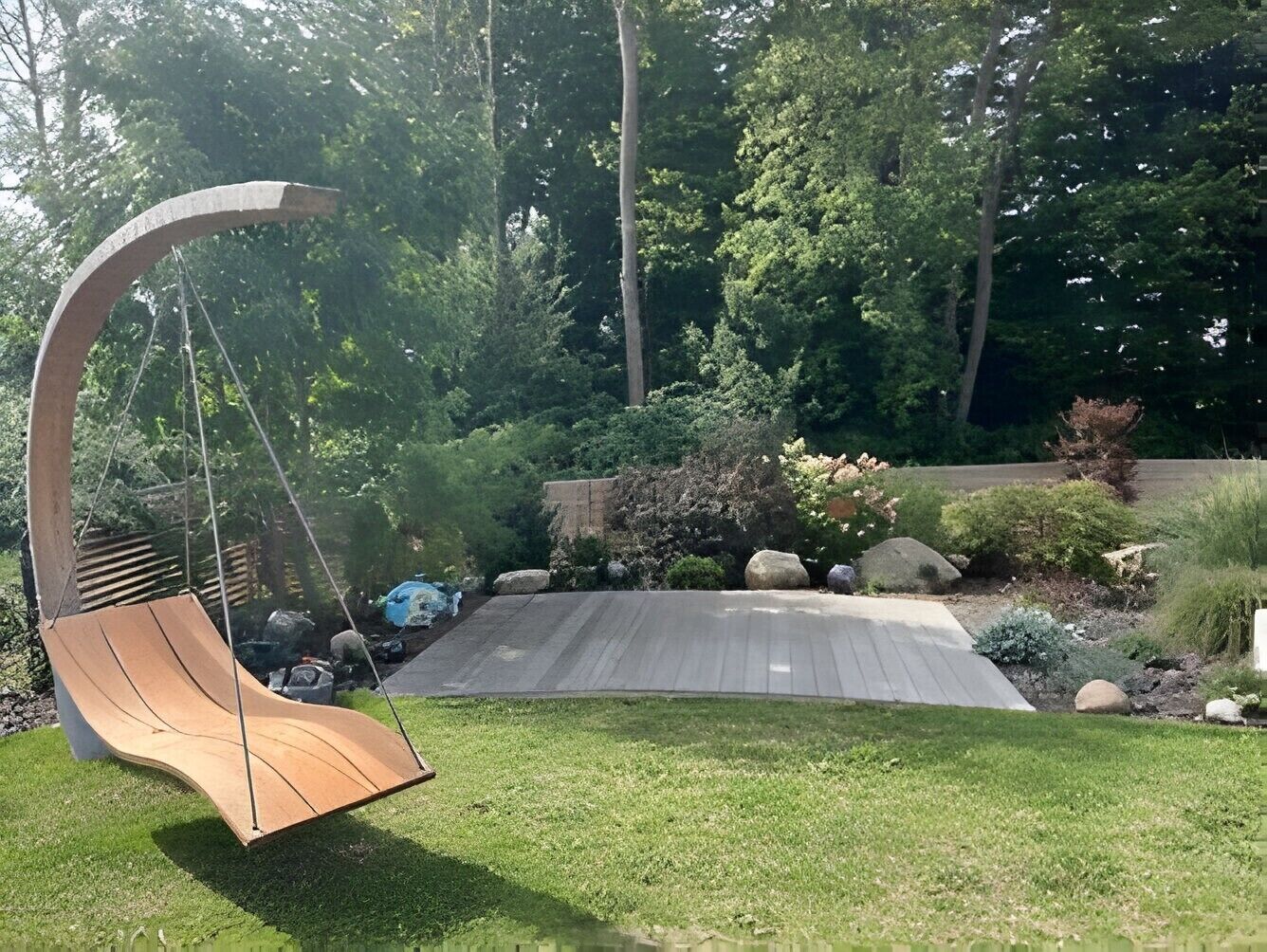 Ein Schaukelstuhl aus Holz in einem Garten mit Holzterrasse, umgeben von viel Grün und Steinen.
