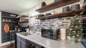 A modern kitchen with a black and white tiled backsplash, stainless steel appliances, and wooden shelves with dishes. - NEW | 2 Blocks to the Beach | Island Cottage | Near UTMB | Pet Friendly | Fenced Yard | Grill |Wifi (Galveston)