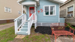 A two-story house with a red door, a white staircase, and a small porch. - NEW | 2 Blocks to the Beach | Island Cottage | Near UTMB | Pet Friendly | Fenced Yard | Grill |Wifi (Galveston)