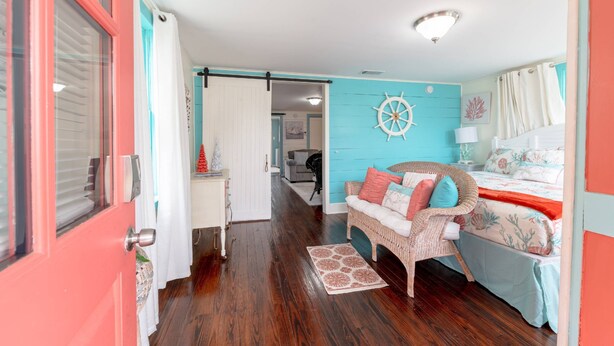 A room with a bed, a wicker chair, a desk, and a door. - NEW | 2 Blocks to the Beach | Island Cottage | Near UTMB | Pet Friendly | Fenced Yard | Grill |Wifi (Galveston)