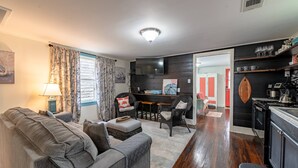 A modern living room with a sofa, chairs, a dining table, and a kitchen area with a stove and shelves. - NEW | 2 Blocks to the Beach | Island Cottage | Near UTMB | Pet Friendly | Fenced Yard | Grill |Wifi (Galveston)