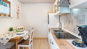 A compact kitchen with a wooden table, white chairs, a coffee machine, and a window with decorative items. - Holiday Apartment "Brigitte" with Mountain View & Wi-Fi (Forbach)