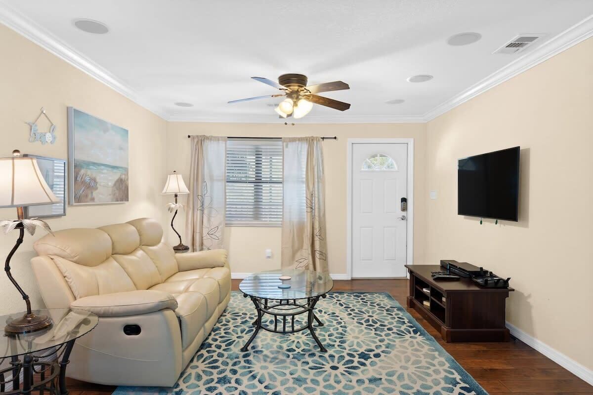 A living room with a leather sofa, a glass coffee table, a ceiling fan, a TV, and a patterned rug.