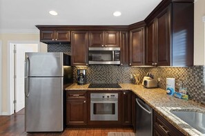 Una cocina con armarios de madera oscura, electrodomésticos de acero inoxidable, encimera de granito y salpicadero de azulejos.