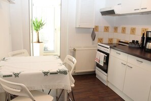 Une cuisine avec des meubles blancs, une cuisinière et une table à manger avec des chaises.