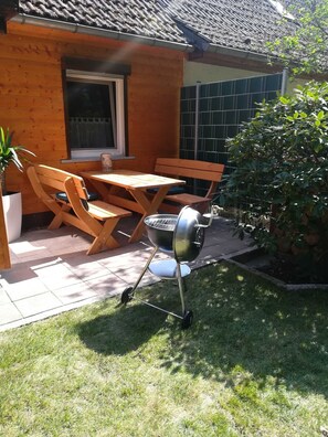 An outdoor patio with a wooden table and chairs, a barbecue grill, and a potted plant. - Studio Apartment 'Ferienwohnung Am Wald' with Private Terrace, Private Garden and Wi-Fi (Michendorf)