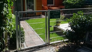 Een gebouw met een pannendak, een omheinde tuin en een bank.