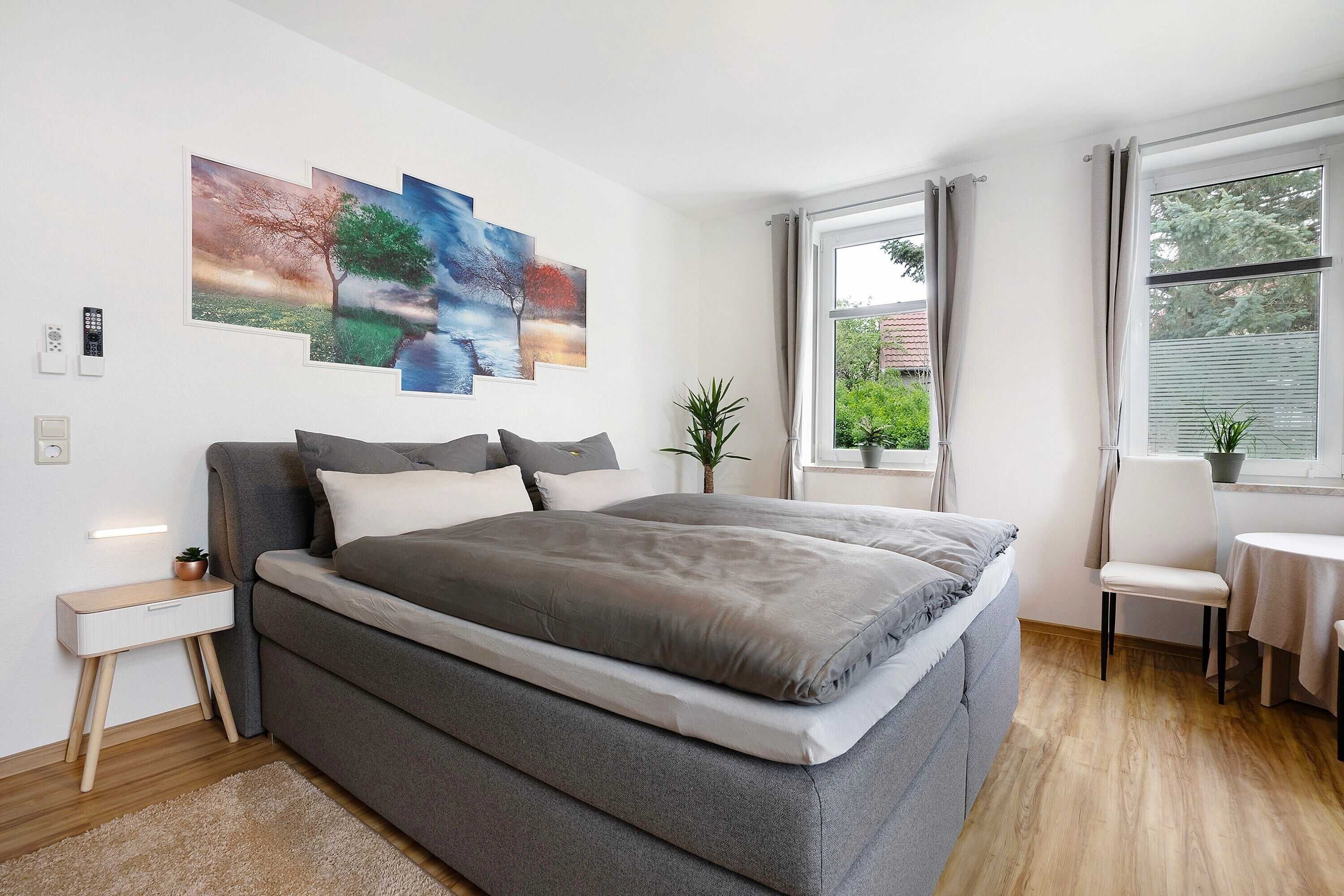 Un dormitorio moderno con una cama grande, una mesita de noche, una planta pequeña y una ventana con cortinas.