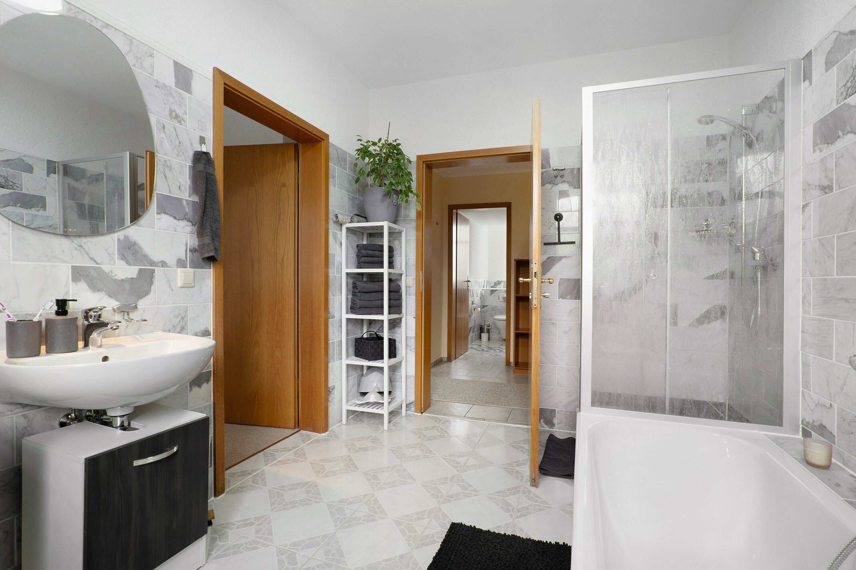 Un baño con un lavamanos blanco, un espejo, una ducha y una puerta de madera.