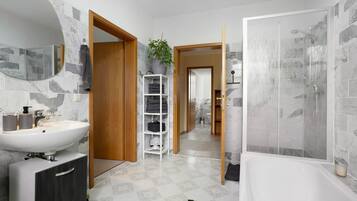 Un baño con un lavamanos blanco, un espejo, una ducha y una puerta de madera.