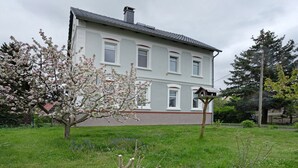 A two-story house with a sloped roof, a chimney, and a small porch with a wooden railing.