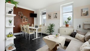 A modern living room with a dining area, a sofa set, and a TV mounted on the wall.