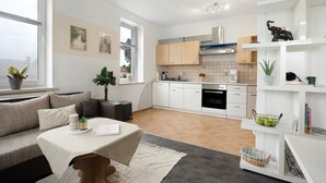 A modern kitchen with white cabinets, a stove, and a sink. There is a dining area with a table and chairs.