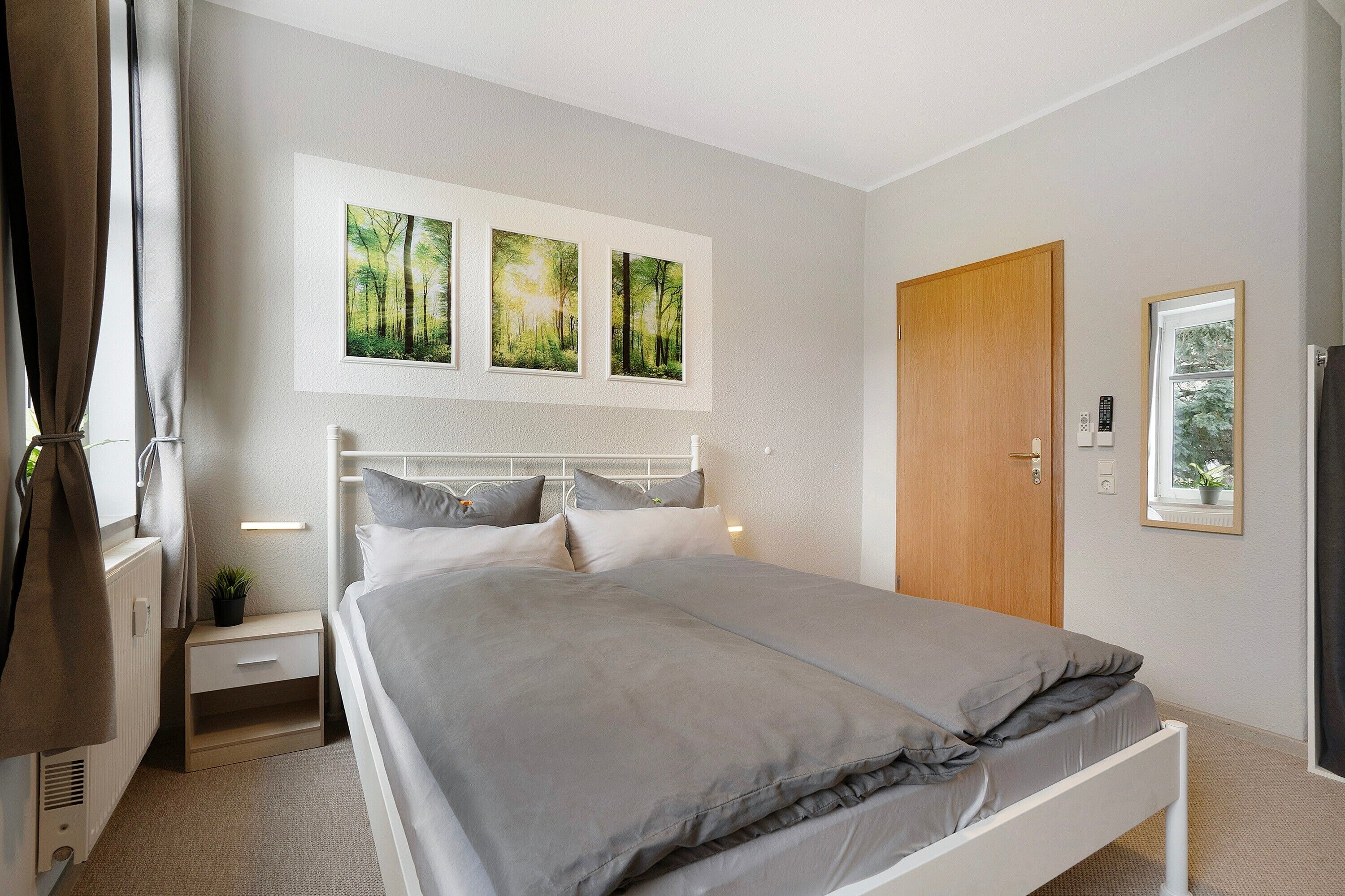 A bedroom with a bed, bedside tables, a nightstand, a wooden door, and three framed pictures on the wall.