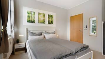 A bedroom with a bed, bedside tables, a nightstand, a wooden door, and three framed pictures on the wall.