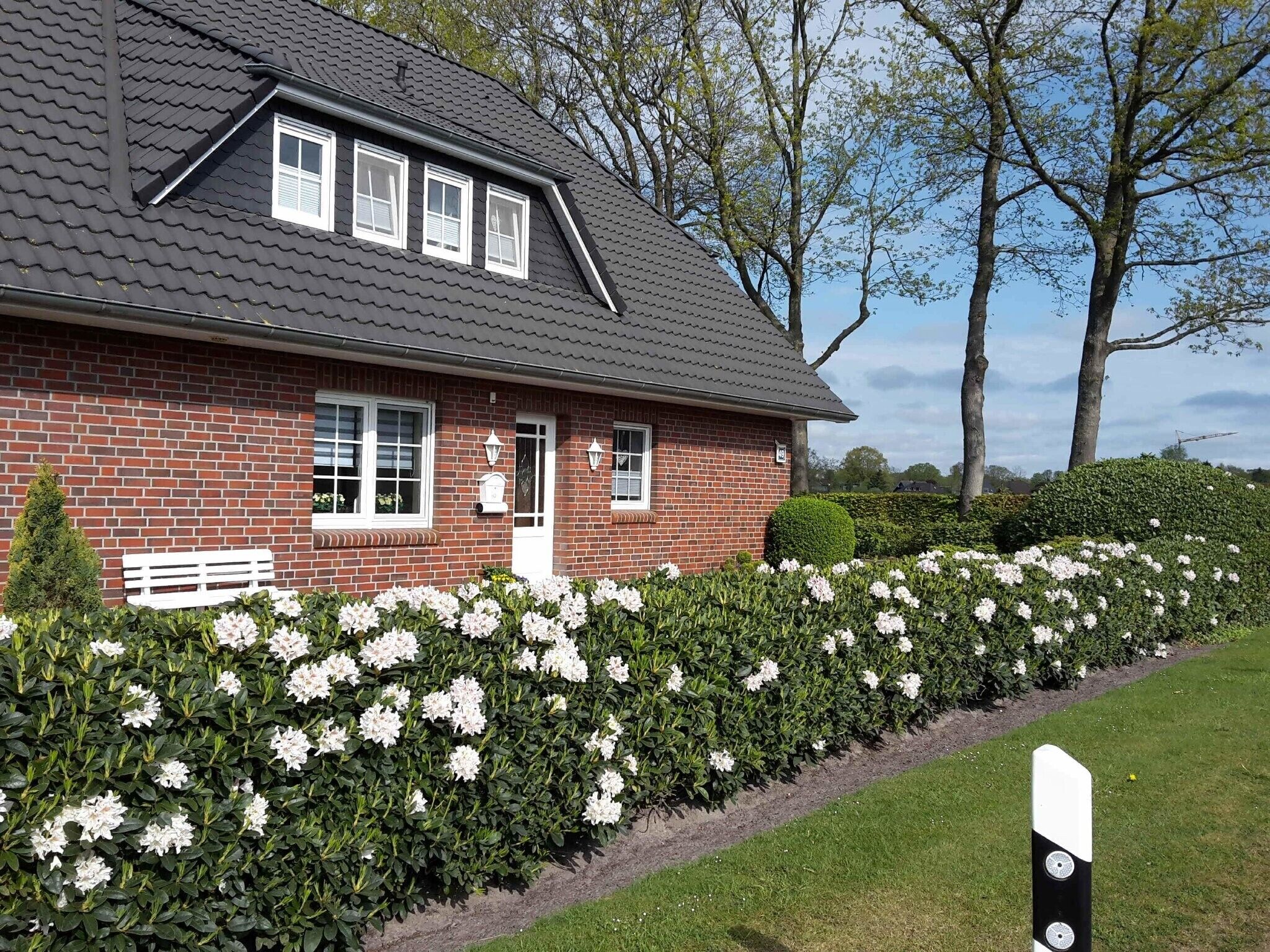 Een bakstenen huis met een schuin dak, witte ramen en een bankje ervoor.