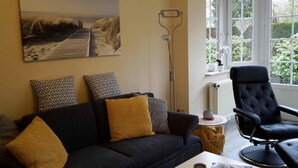 Ein Wohnzimmer mit Sofa, Couchtisch, Sessel, Gemälde, Stehlampe und einem Fenster mit Blick.