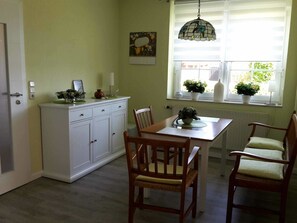 A dining area with a table, chairs, a white cabinet, and a window with plants.