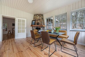 Un comedor con chimenea de piedra, suelo de madera y ventanas amplias.