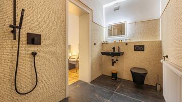 Een moderne badkamer met douche, wastafel en toilet, met een metselwerk wand en een zichtbare deur naar een andere kamer.