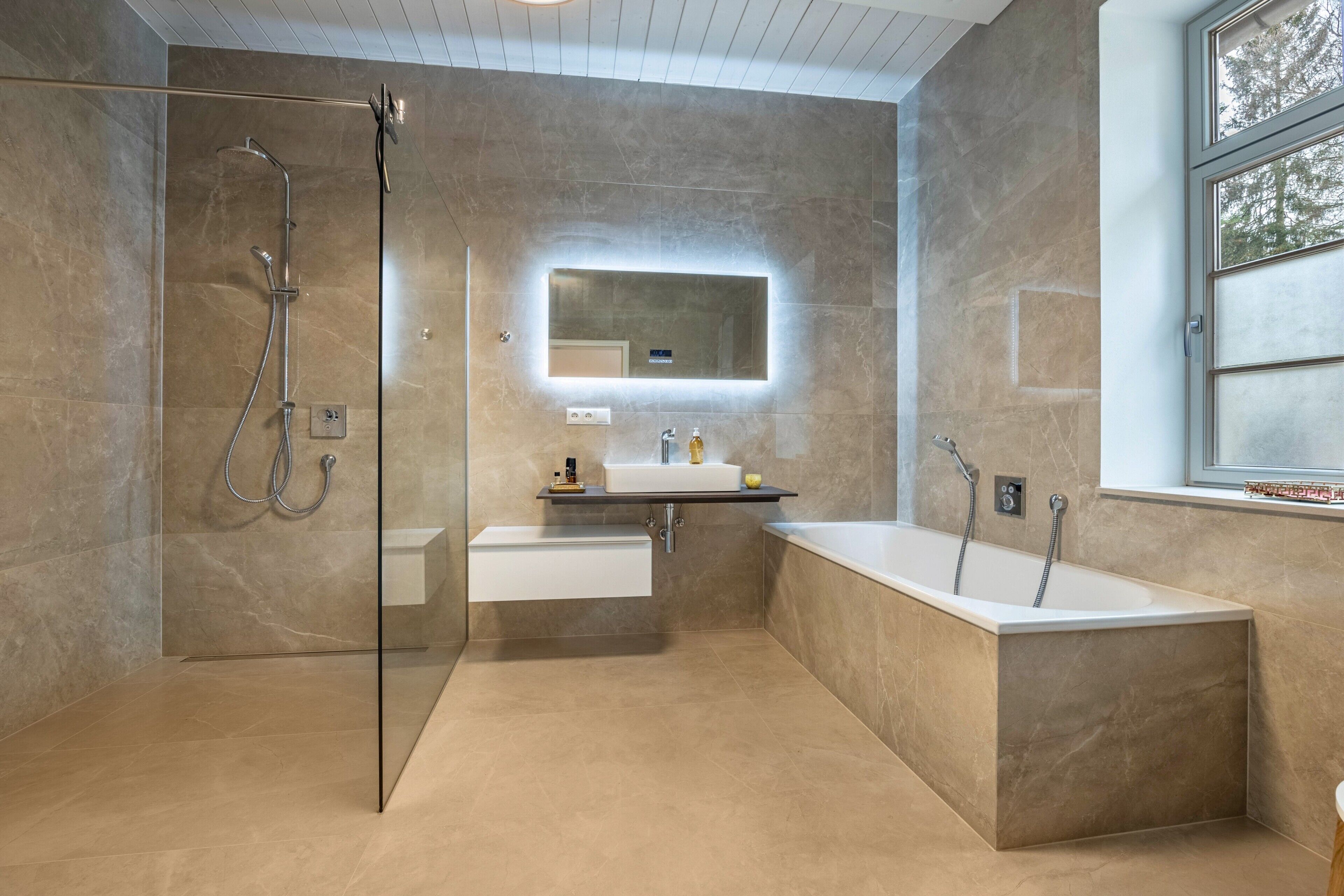Un baño moderno con ducha envuelta en cristal, bañera independiente y tocador con espejo.