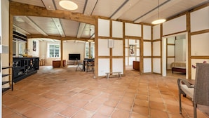 A spacious room with a tiled floor, wooden beams, a black entertainment unit, and a seating area with a chair and table.