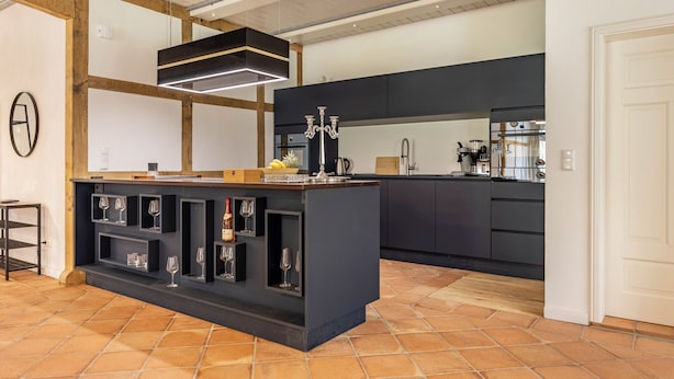 A modern kitchen with a central island, black cabinetry, and a hanging light fixture.