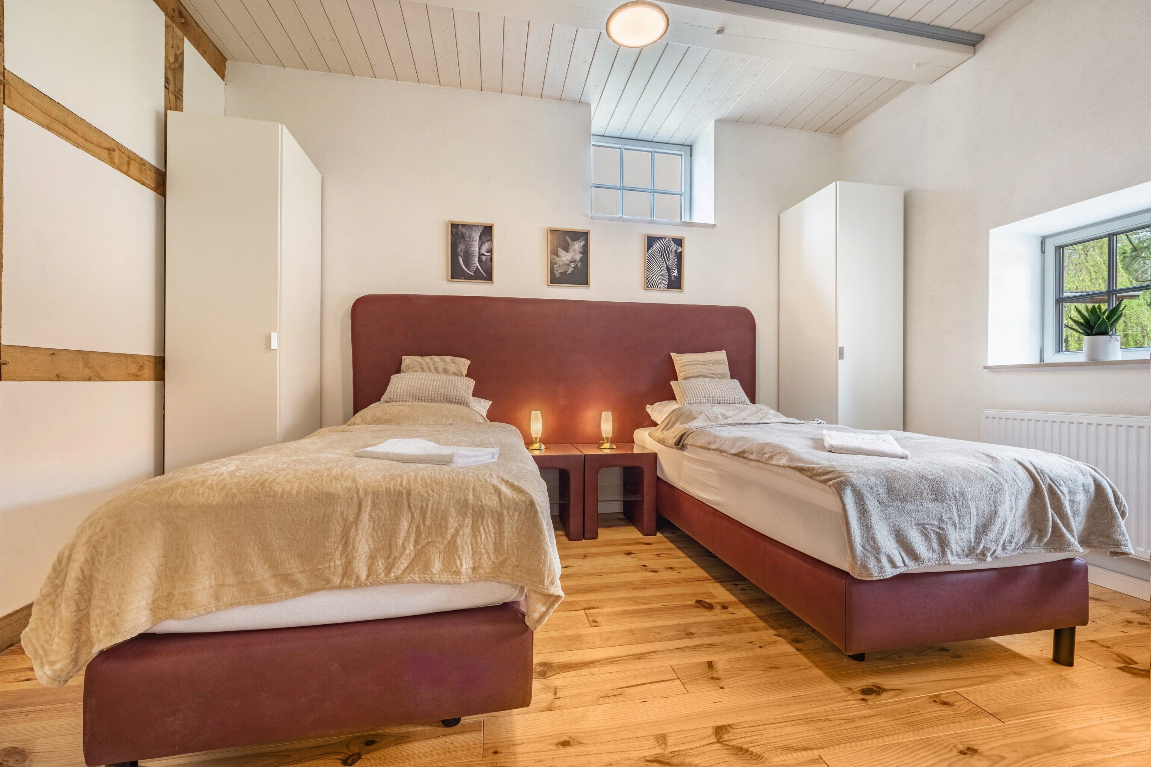 Een slaapkamer met twee bedden, houten vloeren, een raam met een plant en kunst aan de muur.
