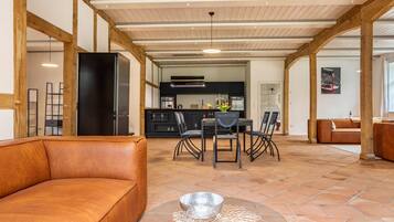 En rummelig opholdsstue med en lædersofa, et glasbord og et spiseområde med stole og bord.