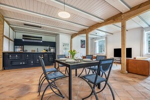 Un comedor amplio con una gran mesa y sillas, una cocina al fondo y una sala de estar con sofá y televisor.
