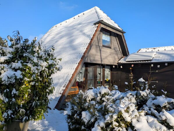 A snow-covered building with a sloped roof, a visible window, and a door.