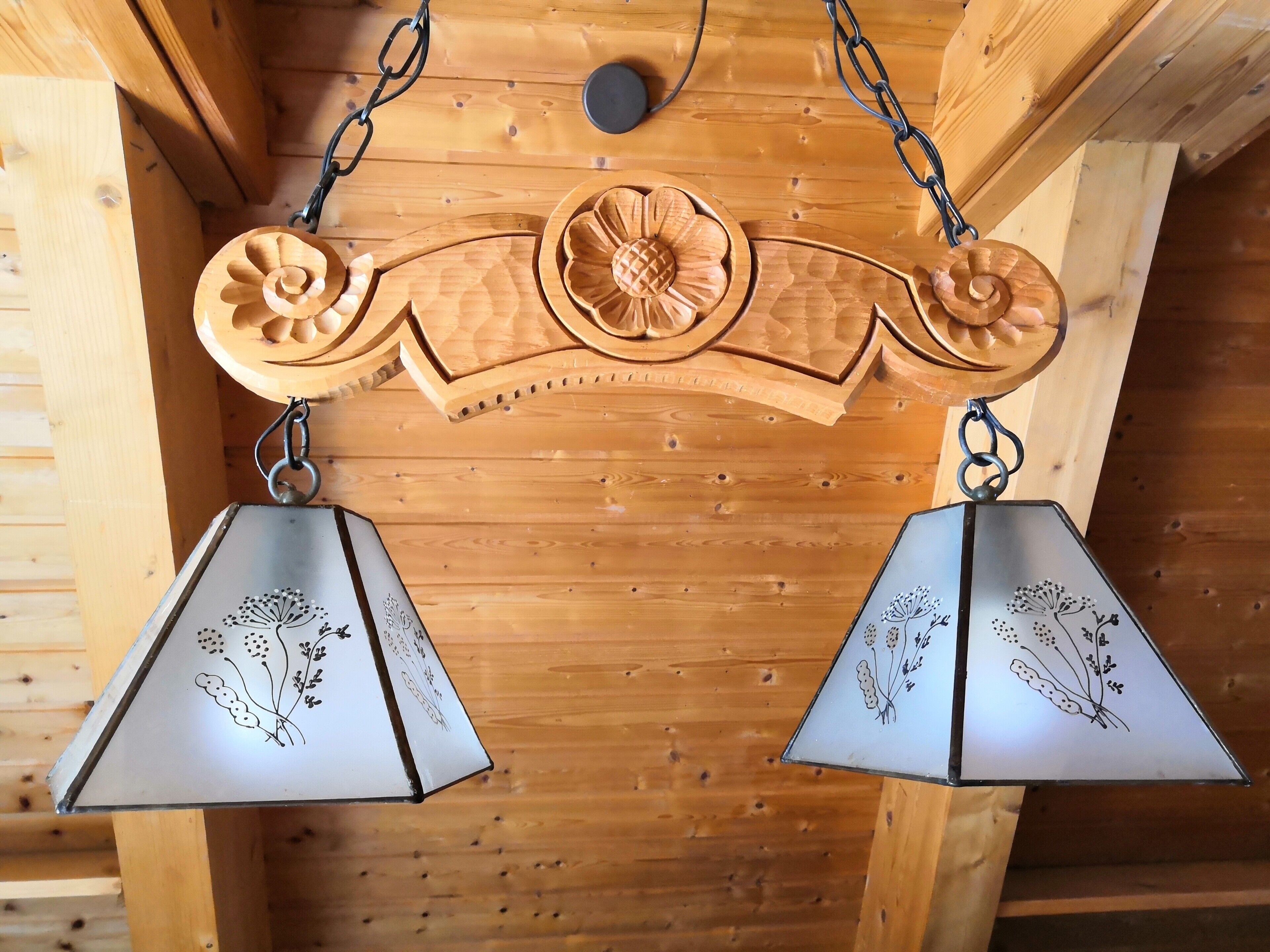 Een houten plafond met een decoratief houten paneel, voorzien van een centraal embleem en twee hanglampen met bloemenmotieven.