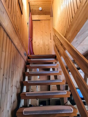 Un escalier en bois, doté d’une rampe, mène à une pièce dont le plafond et les murs sont également en bois.